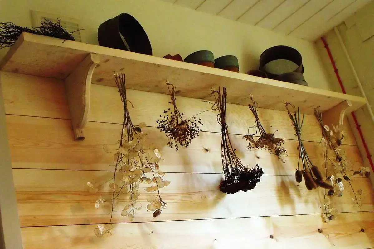 Small bundles of dried flowers hanging beneath a wooden shelf.